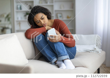 Young Upset Black Woman Looking At Smartphone Screen While Sitting On Couch Young Upset Black Woman Looking At Smartphone Screen While Sitting On Couch 112722039