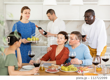 Cheerful friends enjoying wine and conversations in home kitchen 112722099