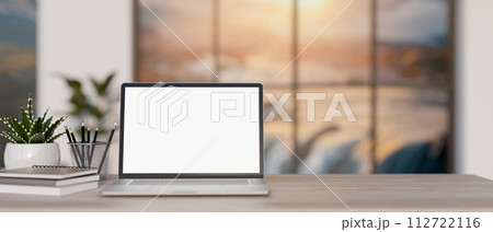 A close-up image of a laptop computer mockup and stationery on a wooden desk in a modern office. 112722116