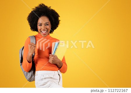 Excited young student with an afro smiling broadly, holding notebooks 112722167