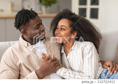 Happy black young couple cuddling sharing embrace in living room Happy black young couple cuddling sharing embrace in living room 112722411