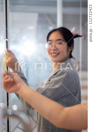 A creative Asian businesswoman reading some ideas on sticky notes while brainstorming with her team. A creative Asian businesswoman reading some ideas on sticky notes while brainstorming with her team. 112722423