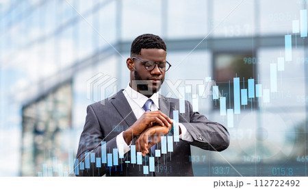 Punctual businessman in a suit checks the time on his watch in front of a glass building 112722492