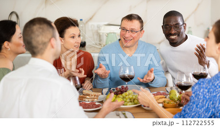 Companions congregated around a festive table, participating in animated discussions and enjoying the delights of red wine Companions congregated around a festive table, participating in animated discussions and enjoying the delights of red wine 112722555