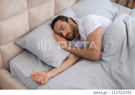 Man peacefully sleeping in comfortable bed with soft pillows 112722591