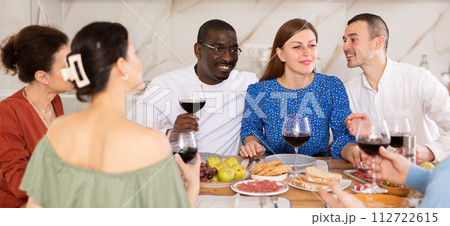 Middle-aged friends sitting at table with a glass of wine while having friendly conversation 112722615