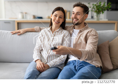 Smiling couple relaxing with remote on sofa, watching tv 112722770