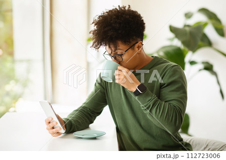 Handsome stylish african american guy drinking coffee, using smartphone 112723006