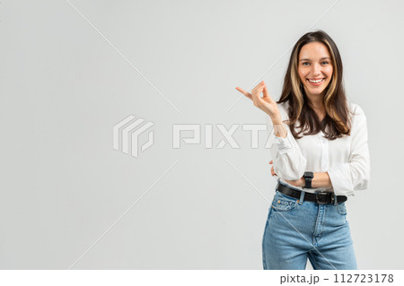 A radiant young woman with brown hair and a white blouse gestures with one hand A radiant young woman with brown hair and a white blouse gestures with one hand 112723178