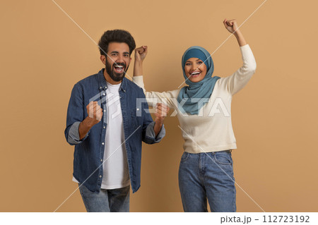 Emotional young muslim couple celebrating success, clenching fists and screaming 112723192