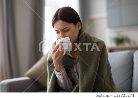 Sick woman with cold, blowing her nose, sitting on the couch 112723271