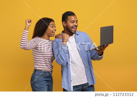 Online Win. Joyful African American Couple Holding Laptop And Celebrating Success 112723312