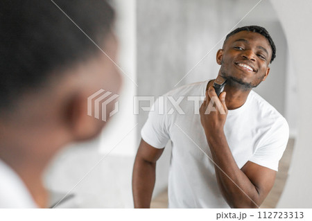 Happy African American man shaving with an electric razor indoor 112723313