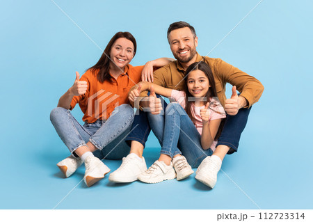 Cheerful parents and daughter making thumbs up gesture, blue background 112723314