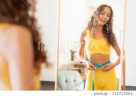 teen girl measures slender waist with tape at home 112723361