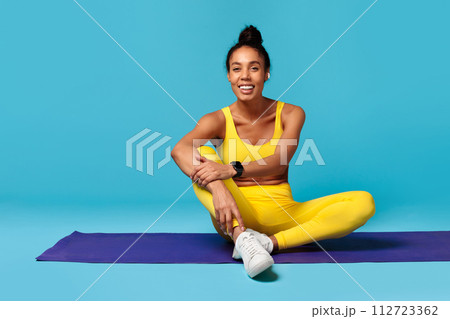 black lady in activewear with tracker sits on mat, studio black lady in activewear with tracker sits on mat, studio 112723362