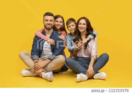 Happy young family of four sitting on floor and embracing Happy young family of four sitting on floor and embracing 112723570