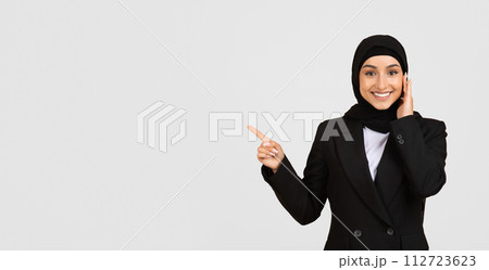 Smiling muslim businesswoman in hijab pointing to the side at free space Smiling muslim businesswoman in hijab pointing to the side at free space 112723623
