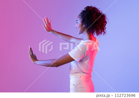 Young lady gesturing with hands on neon vibrant background 112723696