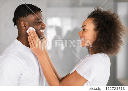 black wife cleansing husband's skin with cotton pads in bathroom 112723718
