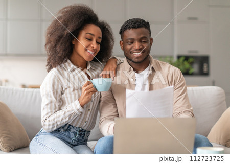 Happy African couple with laptop and papers enjoying coffee indoors 112723725