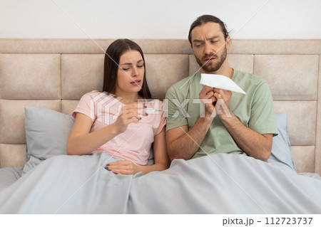 Worried couple with thermometer and tissue in bed 112723737