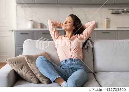 Woman relaxing with hands behind head on couch 112723890
