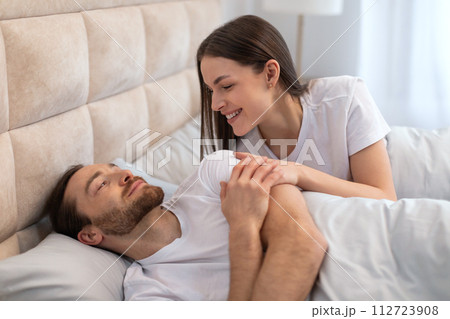 Affectionate woman smiling at her resting partner in bed Affectionate woman smiling at her resting partner in bed 112723908