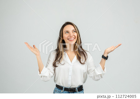 An upbeat young woman in a white blouse and blue jeans is raising her hands, palms up An upbeat young woman in a white blouse and blue jeans is raising her hands, palms up 112724005