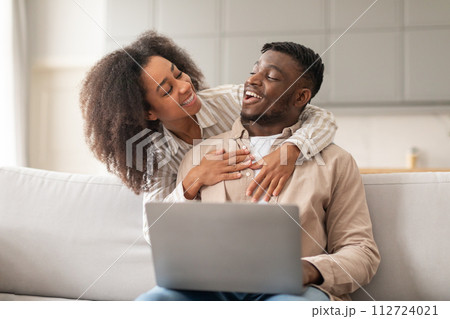 Young African American couple hugs watching movie on laptop indoor 112724021