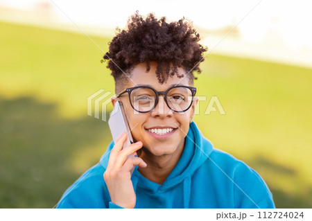 Portrait of smiling black student guy talking on cellphone outdoors 112724024