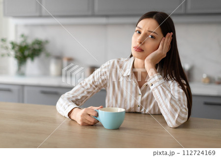 Worried upset woman with coffee cup at kitchen table Worried upset woman with coffee cup at kitchen table 112724169