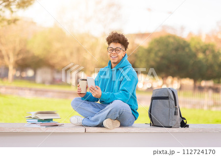 Brazilian university student enjoying coffee and using his smartphone outdoor Brazilian university student enjoying coffee and using his smartphone outdoor 112724170