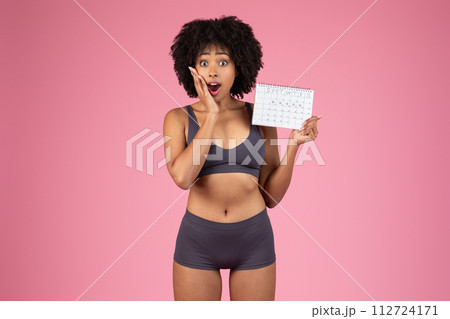 Surprised black woman holding personal tracking calendar Surprised black woman holding personal tracking calendar 112724171