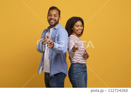 Cheerful young black couple playfully pointing at the camera with confident smiles Cheerful young black couple playfully pointing at the camera with confident smiles 112724268