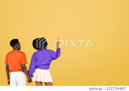 Rear view of a connected young couple, the woman in a purple blouse pointing upwards 112724407