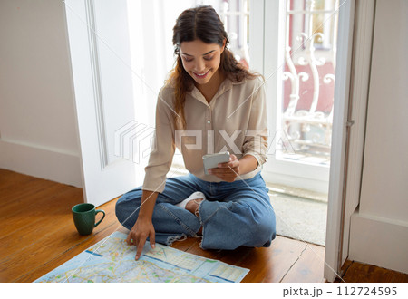 Young woman using her smartphone and city map to plan journey 112724595