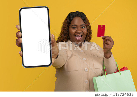 Happy young chubby black woman showing phone and credit card Happy young chubby black woman showing phone and credit card 112724635