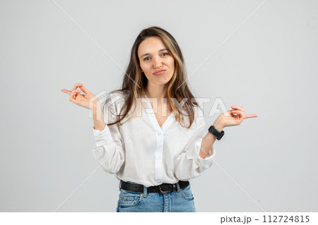 A young woman wearing a white blouse and blue jeans with a smartwatch makes an uncertain expression 112724815