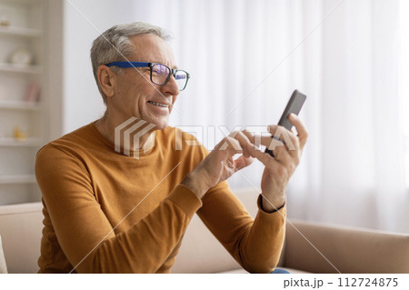 Grandfather wearing eyeglasses using cell phone at home 112724875