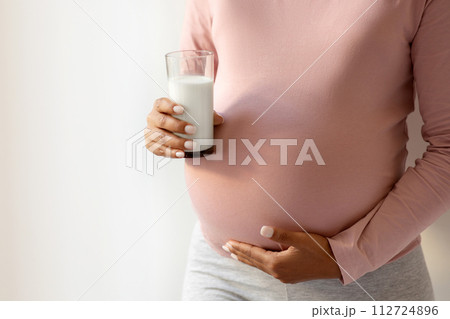 Pregnant woman cradling her belly and holding glass of milk Pregnant woman cradling her belly and holding glass of milk 112724896