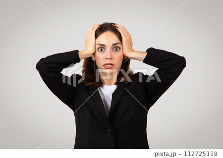 Stressed businesswoman with wide eyes and a worried expression, clutching her head in alarm or frustration Stressed businesswoman with wide eyes and a worried expression, clutching her head in alarm or frustration 112725118