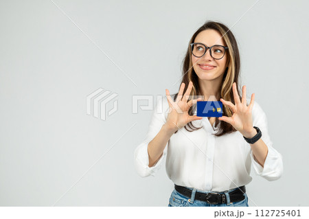 Optimistic young woman with glasses holding a blue credit card between fingers 112725401
