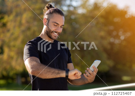 man in sportswear looking at smartwatch holding mobile phone outside man in sportswear looking at smartwatch holding mobile phone outside 112725407