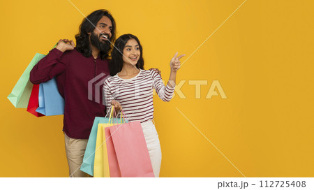 Excited young indian couple shopping together, pointing at copy space Excited young indian couple shopping together, pointing at copy space 112725408