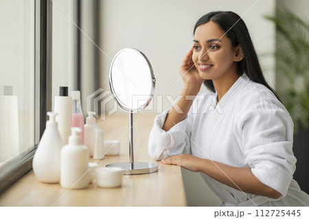 Pretty young indian woman looking at mirror, touching her skin Pretty young indian woman looking at mirror, touching her skin 112725445