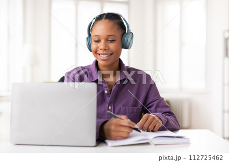 Lady student with headphones taking notes during an online class 112725462