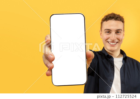 Cheerful young man showing smartphone with blank display Cheerful young man showing smartphone with blank display 112725524