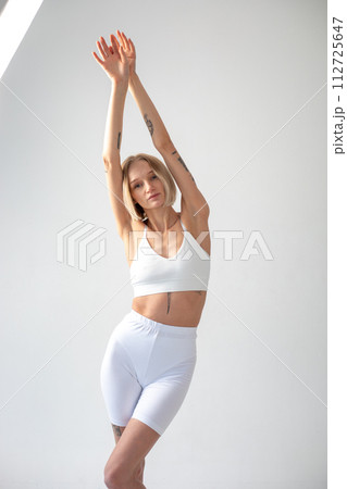 Blonde girl posing on a white background in a top and leggings Blonde girl posing on a white background in a top and leggings 112725647