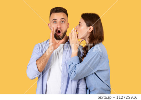Shocked man looking at camera while woman whispering secret 112725916